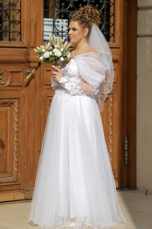 Woman in a bridal dress with floral lace applications and sheer, flowing sleeves